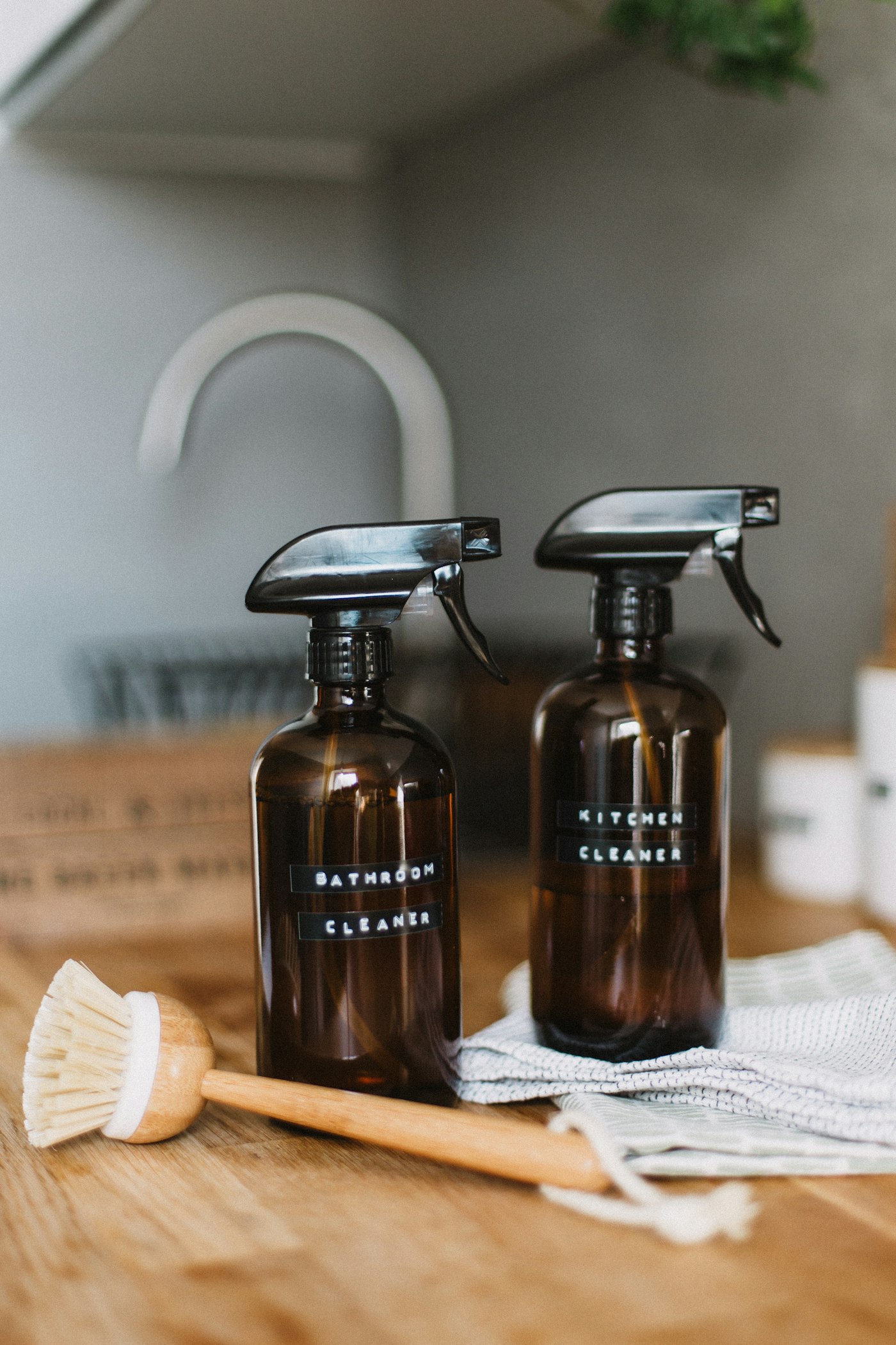 Amber-glass spray bottles and a wooden brush on a kitchen counter